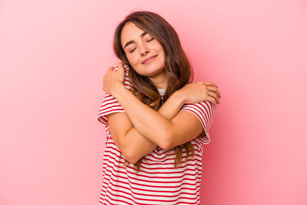 joven mujer caucasica aislada sobre fondo rosa abrazos sonriendo despreocupada